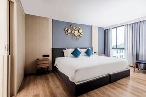 A modern hotel room with a large bed, a nightstand, a wall-mounted decorative piece, and a view of the outdoors through the window. - Duplex Liora 1br Pools|gym & shuttle to nai harn (Rawai)