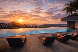 A swimming pool with lounge chairs and a sunset view.