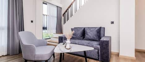 Una sala moderna con un sofá gris, un sillón gris y una pequeña mesa blanca con un florero.