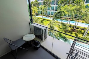 A balcony with a table and chairs, overlooking a swimming pool and greenery.