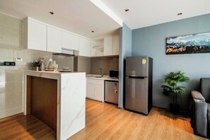 Eine moderne Küche mit weißen Schränken, einer Marmorinsel, einem Edelstahlkühlschrank und einem Essbereich mit grauem Sofa.
