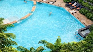A swimming pool with a curved design, surrounded by lounge chairs and palm trees. - Suite Nami 1br | Pools|gyms & shuttle to nai harn (Rawai)