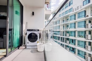 A balcony with a washing machine, a mop, and a basket. - Suite Nami 1br | Pools|gyms & shuttle to nai harn (Rawai)