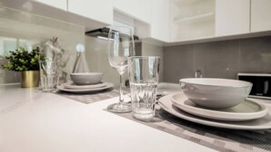 A modern kitchen with white cabinets, a dining table set with clear glasses and white plates.
