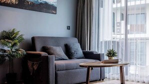 A modern living room with a grey sofa, a round wooden coffee table, and a potted plant. - Suite Nami 1br | Pools|gyms & shuttle to nai harn (Rawai)