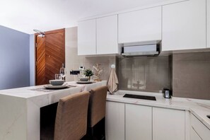 A modern kitchen with white cabinets, a marble countertop, and a built-in stove. - Suite Nami 1br | Pools|gyms & shuttle to nai harn (Rawai)