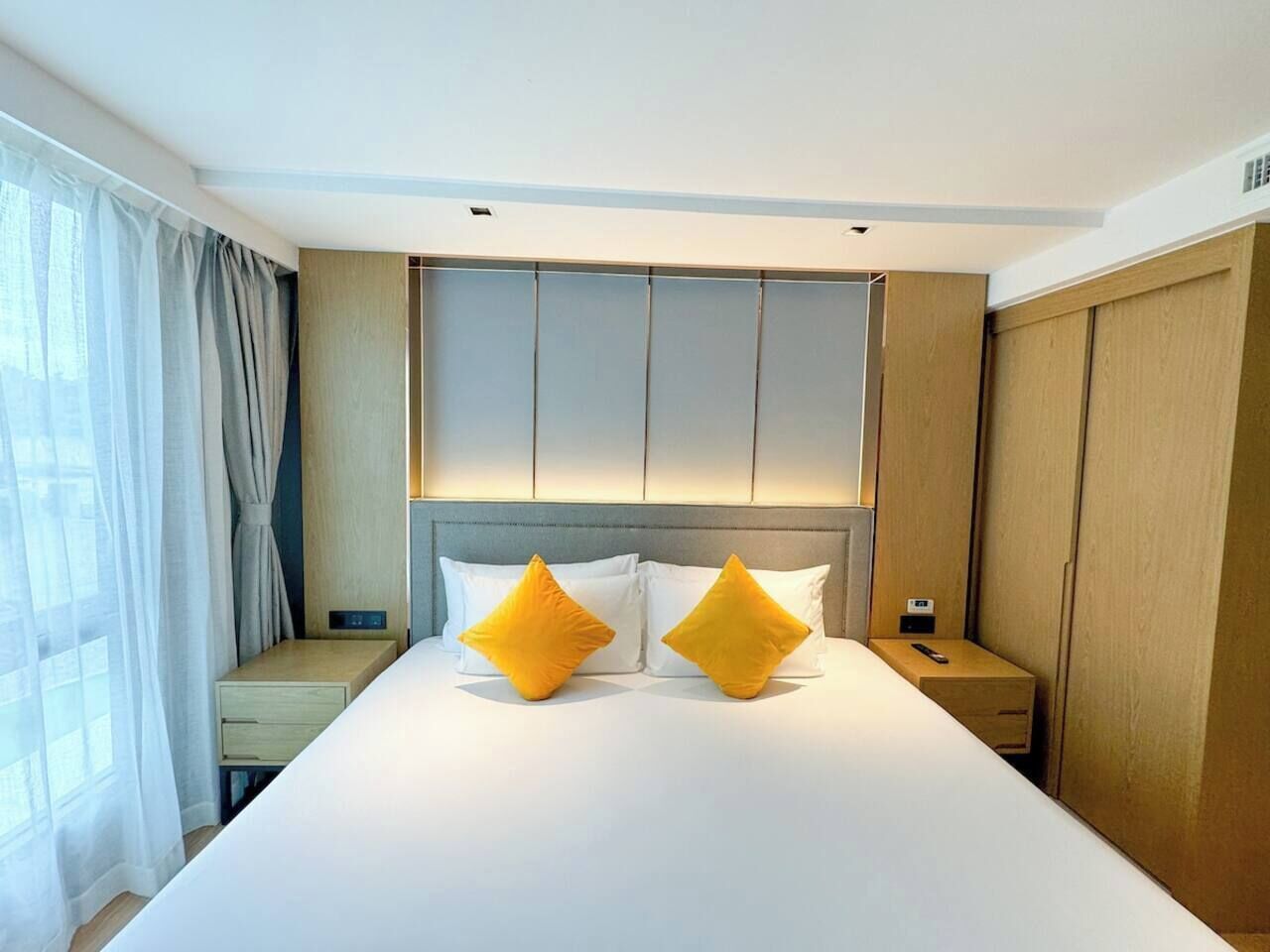 Una habitación de hotel con una cama grande, dos mesitas de noche y un armario.