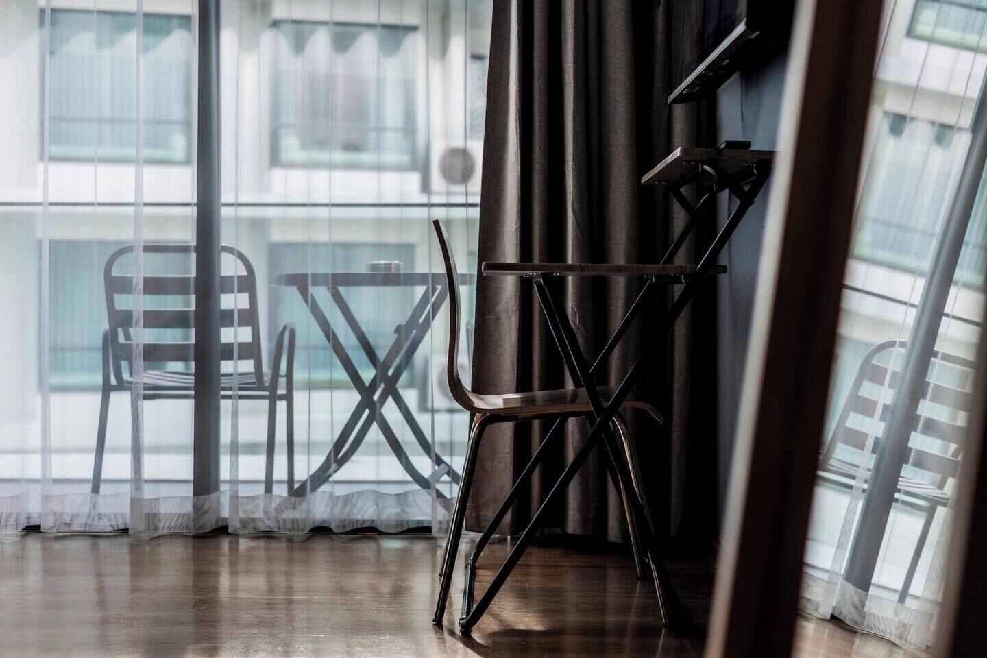 A room with a view through sheer curtains, a foldable chair, and a table.
