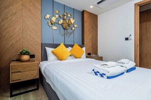 A neatly made bed with white bedding and two yellow pillows, a bedside table with a plant and a remote control, and a wall-mounted decorative piece. - Suite Edena 2br | Pool view | 300m to rawai (Tambon Rawai)