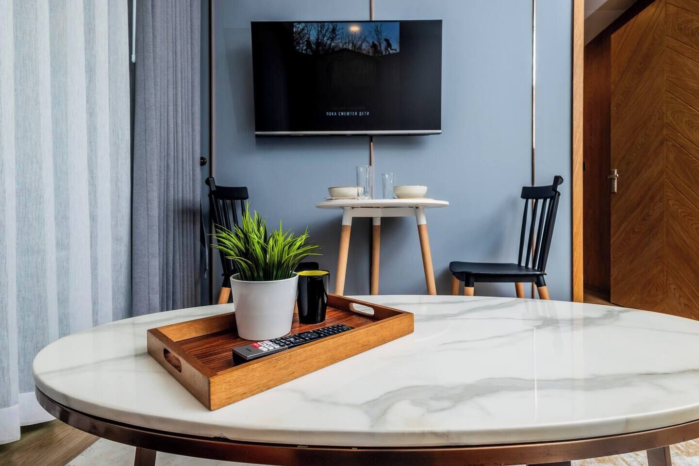 Un espace repas moderne avec une table en marbre, une plante en pot, un plateau avec une télécommande et un téléviseur fixé au mur.