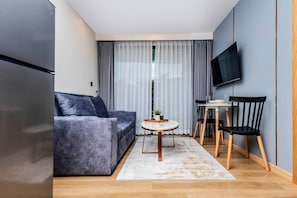 Un espacio habitable compacto con sofá, una mesa de comedor, sillas, televisor y refrigerador.