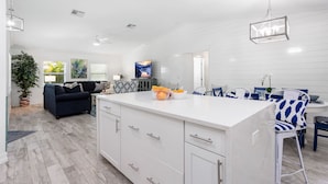 A modern kitchen with white cabinetry, a central island, and a dining area with blue and white chairs.