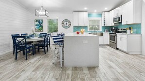 A modern kitchen with white cabinets, a central island, and a dining area with blue chairs.