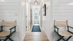 A hallway with white walls, wooden flooring, and two green folding chairs.