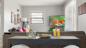 Un salon avec un canapé, une table basse, un téléviseur et une fenêtre avec des stores.