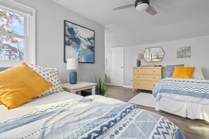 Un dormitorio con dos camas, una mesita de noche, un aparador, un ventilador de techo y un cuadro abstracto grande.