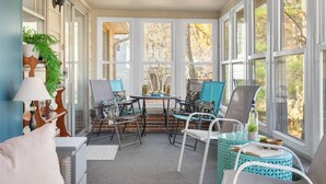 Une véranda donnant sur les arbres, une table avec des chaises et une plante en pot.