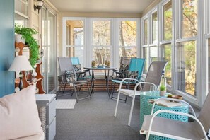 A sunroom with a view of trees, a table with chairs, and a potted plant.
