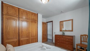 Quarto com cama grande, guarda-roupa de madeira, cômoda e espelho na parede.