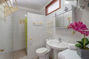 Une salle de bain Ă©quipĂ©e de toilettes, dâun lavabo, dâune douche et dâune orchidĂ©e en pot.