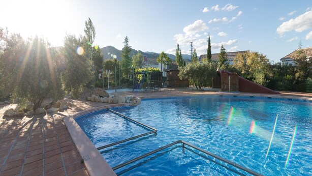 A swimming pool with a clear sky, trees, and buildings in the background. - 2-bedroom Ibipozo Home With Pool (Pozo Alcon)