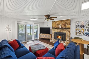 A living room with a stone fireplace, a television, and a ceiling fan.