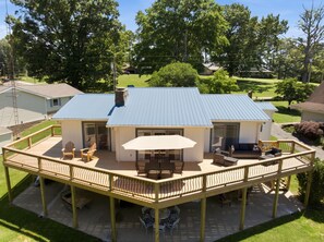 A two-story house with a blue roof, a covered patio with outdoor furniture, and a fenced deck.
