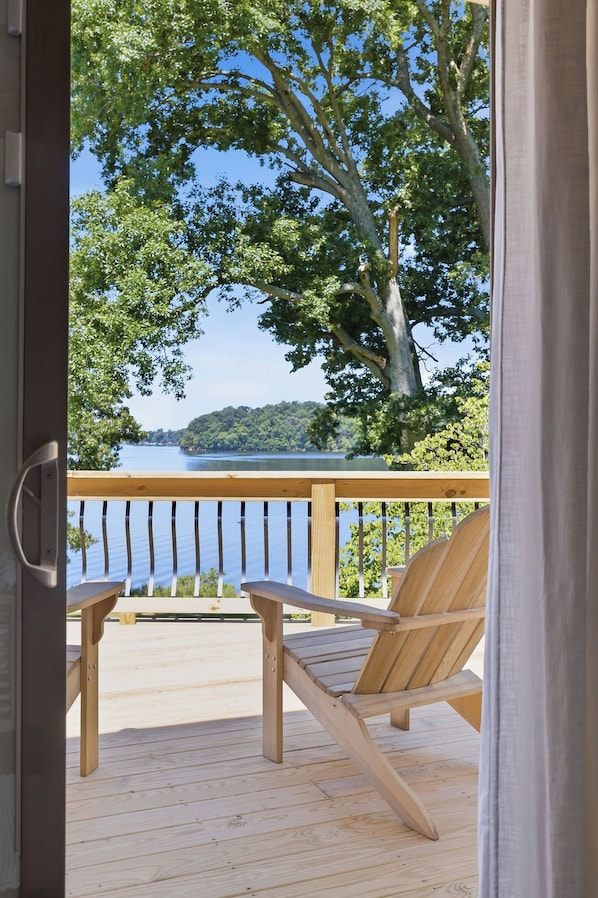 A wooden deck with a chair, a view of a lake, and a forested hill in the background.