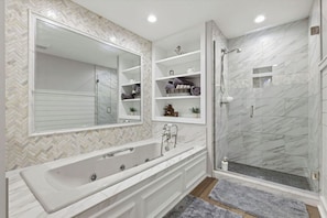 A modern bathroom with a large bathtub, a walk-in shower, and a built-in vanity with shelves.
