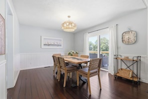 A dining area with a wooden table and chairs, a chandelier, a clock, and a view through a glass door.