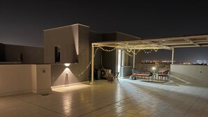 A rooftop terrace with tiled flooring, a covered seating area with chairs, and string lights.
