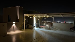 An outdoor patio area with a covered seating area, string lights, and a lamp post.
