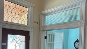 Un pasillo con una puerta de madera, una puerta de vidrio y vista a una habitación con pared azul y una pequeña mesa.