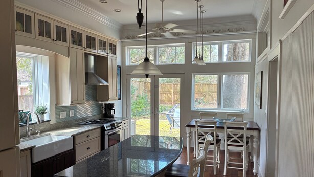Una cocina amplia con isla central, muebles blancos y vista al patio trasero.