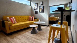 Un salon moderne avec un canapé jaune, deux tables rondes et un tabouret jaune.