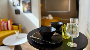 Un coin repas avec une table noire dressée pour deux personnes, agrémenté d’un bol et d’un verre à vin.