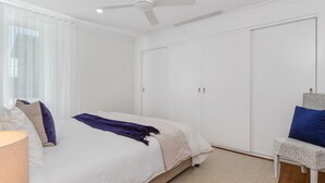 A bedroom with a bed, a wardrobe, a chair, and a ceiling fan. - 2br - Little Opulence Beach Villa on Marine (Kingscliff)