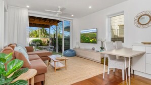 A modern living room with a sofa, coffee table, and a dining area with a table and chairs. - 2br - Little Opulence Beach Villa on Marine (Kingscliff)