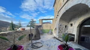 Une cour bordée de murs en pierre, agrémentée d’une pergola et de plantes en pot.