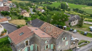 Un bâtiment en pierre, surmonté d’un toit en tuiles, entouré de verdure et situé dans une vallée.