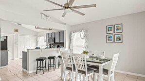 Een moderne keuken met witte kasten, een centraal eiland en een eetgedeelte met witte stoelen.