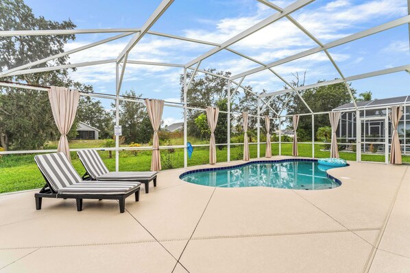 A covered outdoor swimming pool with lounge chairs and a glass enclosure. - The Sunny Spot Home for 8 (Davenport)