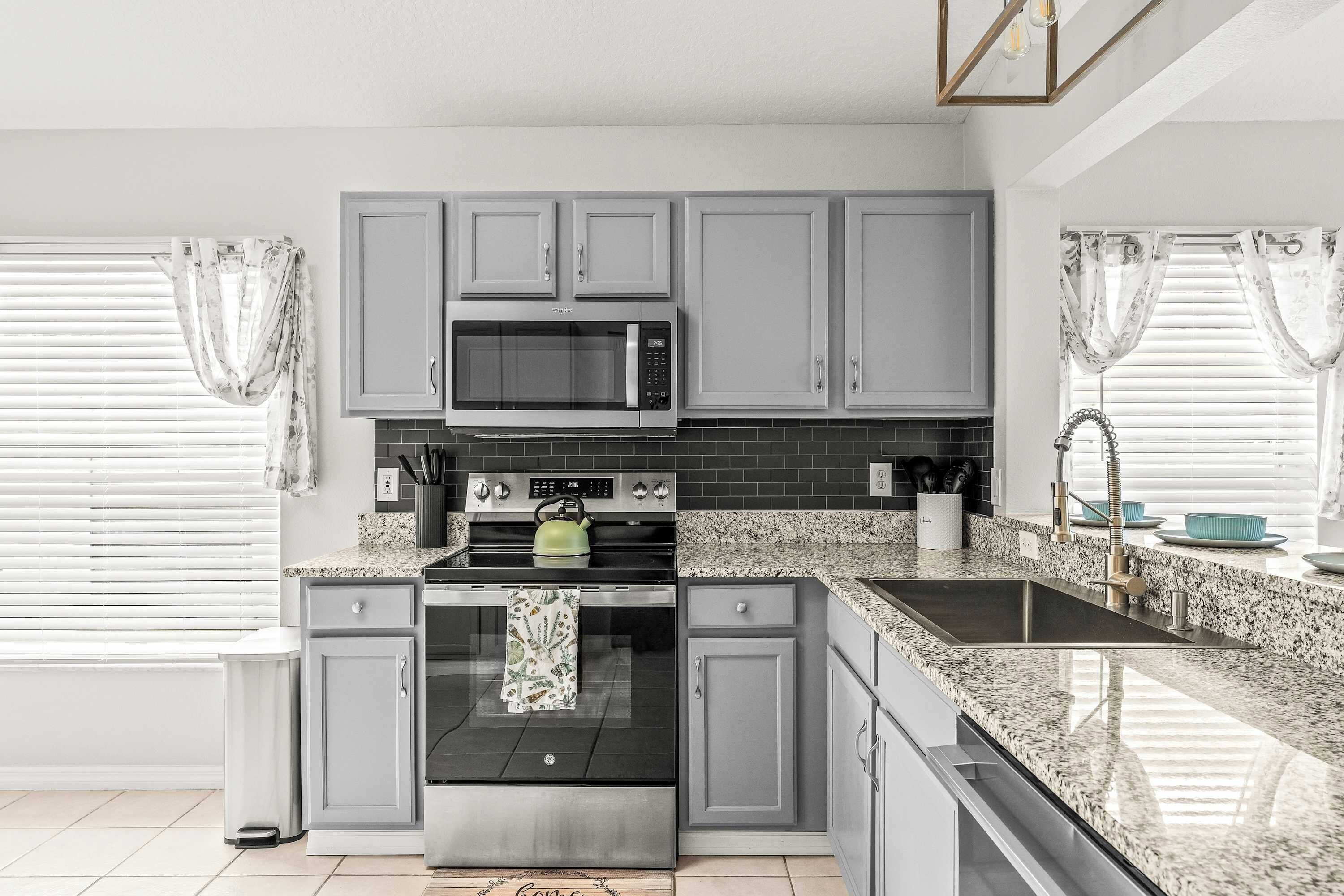 A modern kitchen with grey cabinets, a stainless steel microwave, a built-in oven, and a granite countertop.