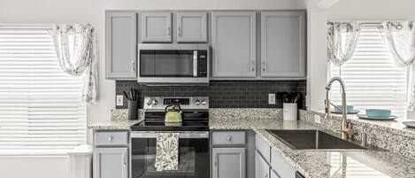 A modern kitchen with grey cabinets, a stainless steel microwave, a built-in oven, and a granite countertop.