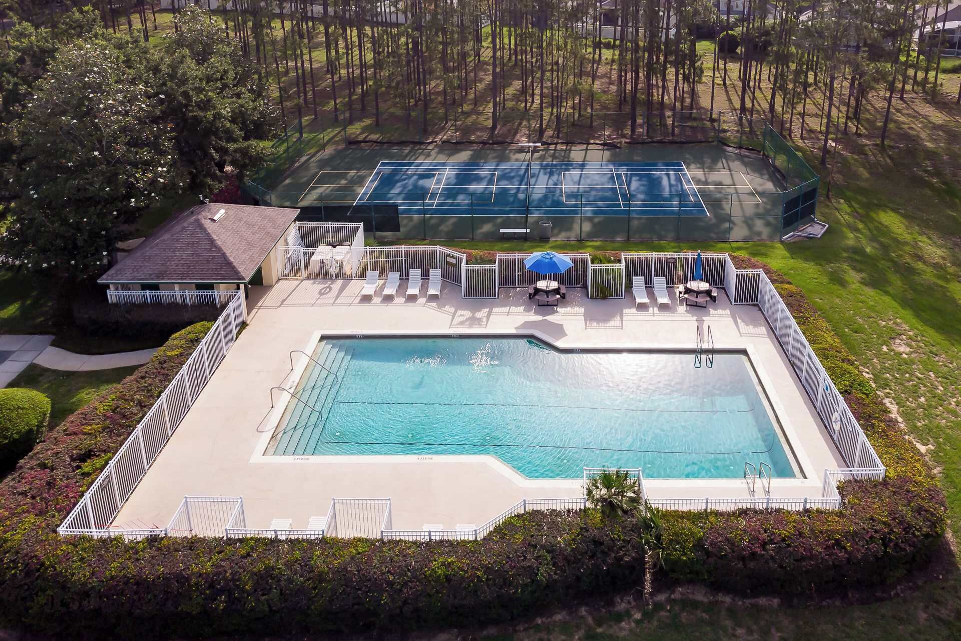 An aerial view of a residential property with a swimming pool, tennis court, and lounge area with umbrellas.