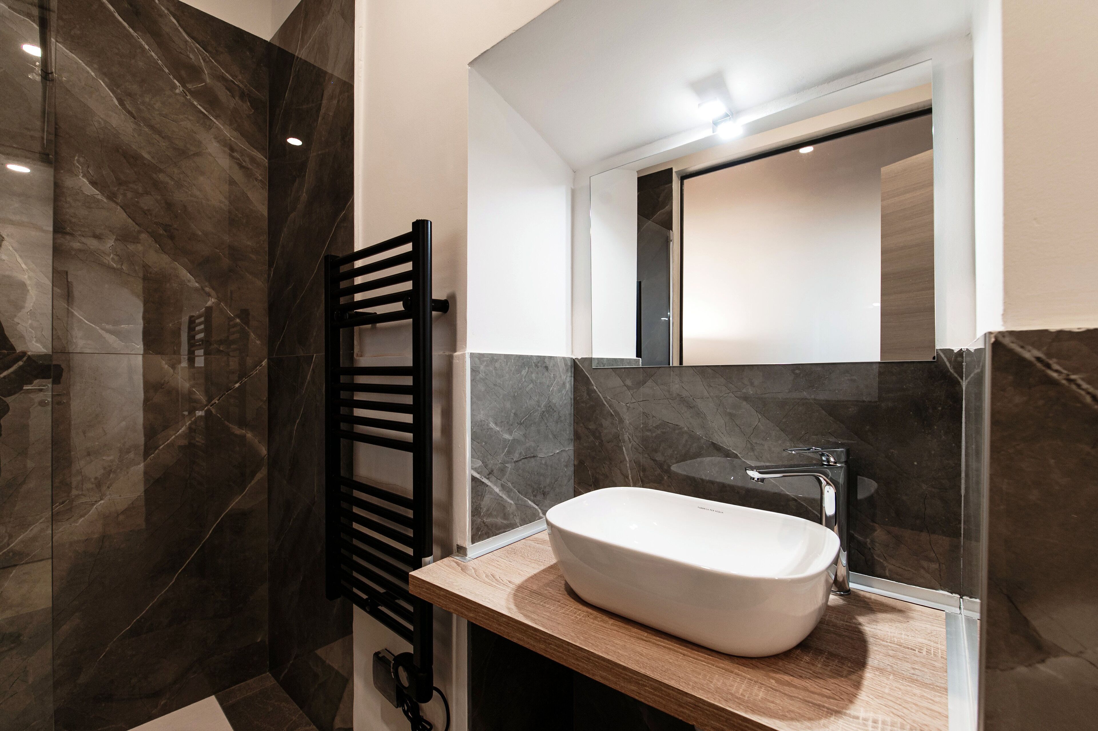 A modern bathroom with a large mirror, a white sink, and a black towel rack.