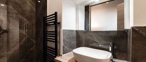 A modern bathroom with a large mirror, a white sink, and a black towel rack.