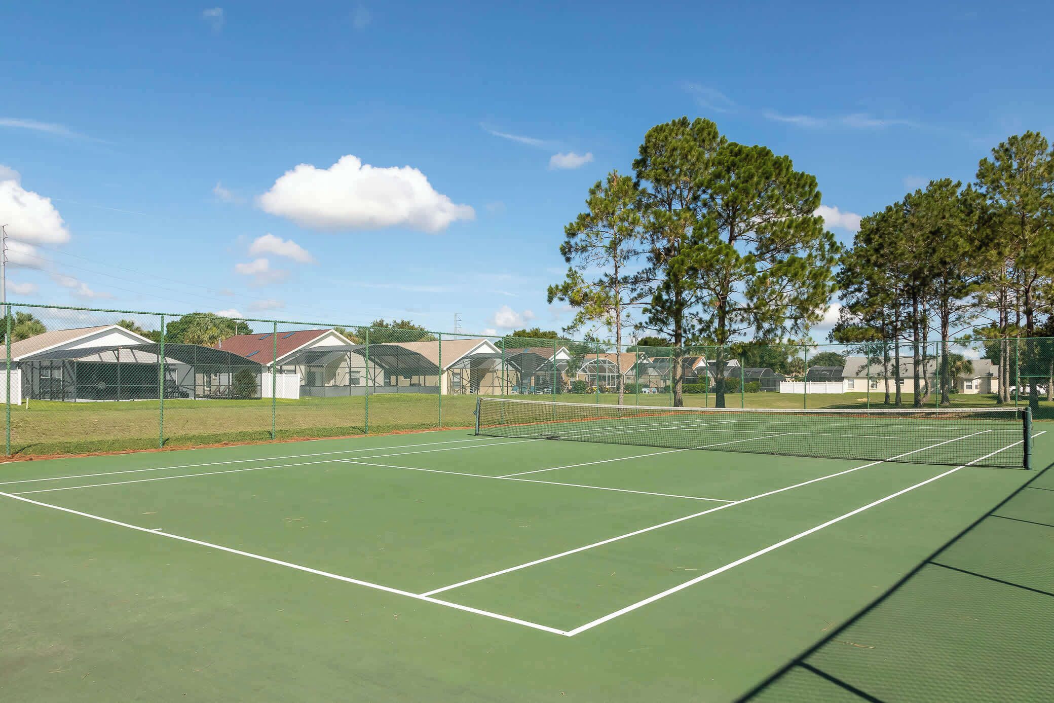 Un court de tennis avec un filet, entouré d’une clôture et d’arbres.
