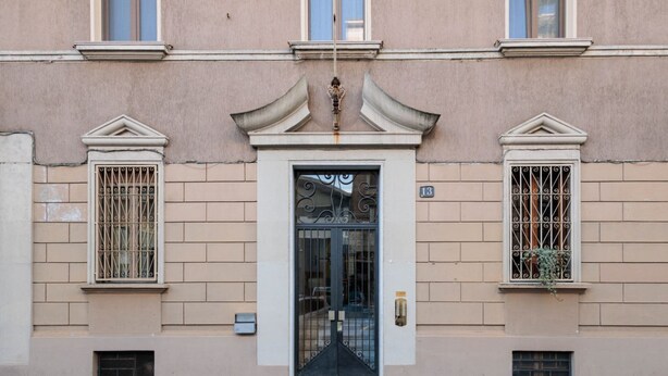 A building facade with a central entrance, flanked by two windows with decorative grills, and a small plant hanging from the right window. - Modern three-room apartment in Via Lambrate, 13 - Mirable PM (Milano)