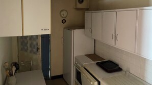 Een compacte keuken met witte kastjes, een witte koelkast, een fornuis en een klok aan de muur.
